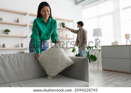 Young Asian woman putting pillow on comfy sofa, making home cozy and warm together with her boyfriend, free space. Millennial couple decorating or designing their apartment Royalty-Free Stock Photo #2094228745