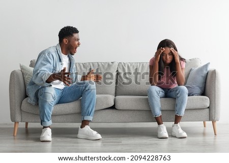 Relationship Problems Concept. Emotional annoyed stressed black couple arguing at home sitting on couch. Angry irritated nervous guy shouting at shocked and frustrated gaslighted lady, fighting Royalty-Free Stock Photo #2094228763