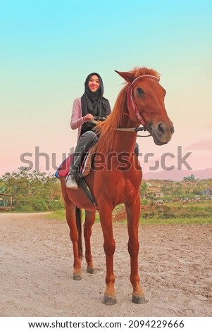 Asian Muslim woman riding horse in countryside