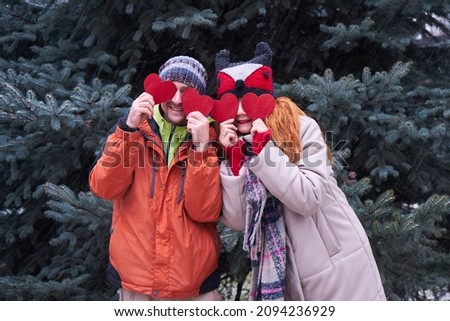 Valentines day concept.Happy young couple is holding red paper hearts and smiling outdoor on Christmas tree background.Couple in valentine day hugging over isolated background                         