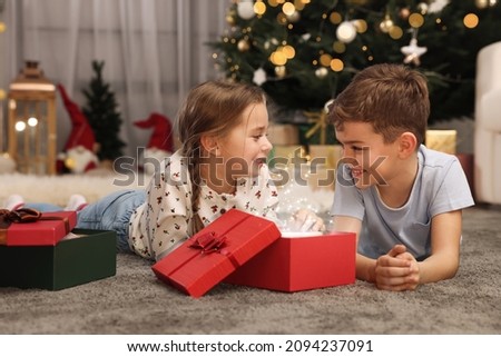 Cute little children opening gift box near Christmas tree at home