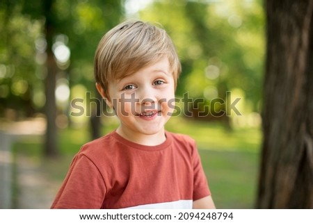 Joyful little boy. He is smiling on the background of a green park. The boy looks into the camera lens Royalty-Free Stock Photo #2094248794