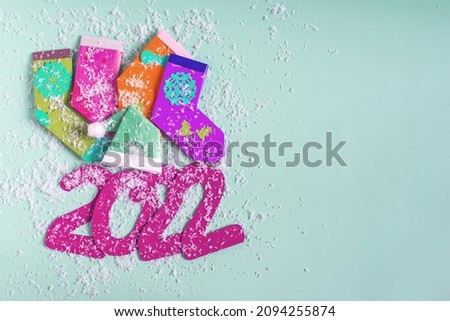Bright Christmas decor, colored socks, a Christmas hat and the numbers 2022 in artificial snow on a colored background is a place for texting.	