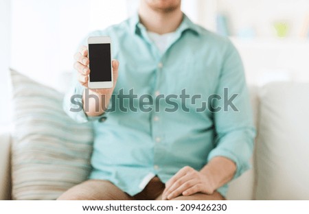 communication, business, home and technology concept - close up of man showing smartphone screen sitting on couch at home
