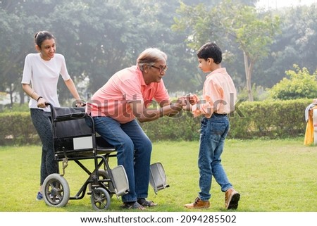 Senior man trying to get up from wheelchair with the help of grandson and granddaughter at park
