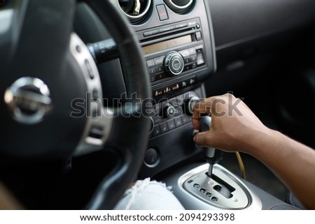 Close-up of a black man's hand in casual clothes at the wheel of a car, shifting gears in a car. An African man drives a automobile