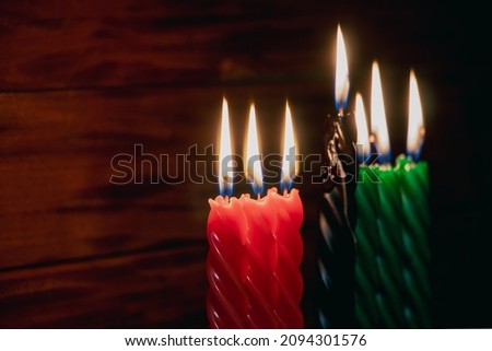 Happy Kwanzaa. African American holiday. Seven burning candles, red, black and green, in kinara candlestick. Symbols of African heritage.