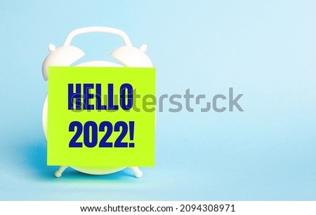 On a blue background - a white alarm clock with a yellow sticker for notes with the text HELLO 2022