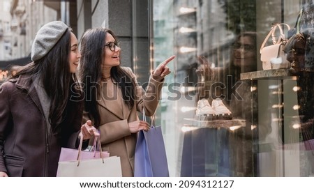 Two young beautiful women females girlfriends enjoy shopping while pointing finger in the shopwindow. Discount and sale, black friday. Shopping for clothes. Royalty-Free Stock Photo #2094312127