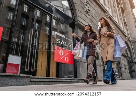 Friends female women walking with shopping bag near Sale sign on shop showcase. Total discount sale, low prices on black friday