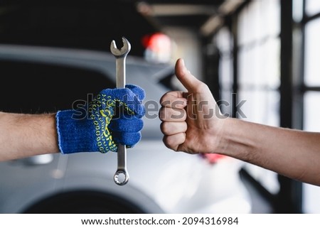 Closeup cropped shot of wrench in technician mechanic hands while male hand showing thumb up. MOT. Vehicle inspection. Repairing fixing car tires wheels at garage workshop service station. Royalty-Free Stock Photo #2094316984