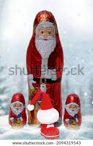 Closeup of various cheerful wrapped chocolate Santa and a Santa Claus boot with a hat over festive abstract blurred winter landscape. Xmas and New Year gift sweets. Macro.