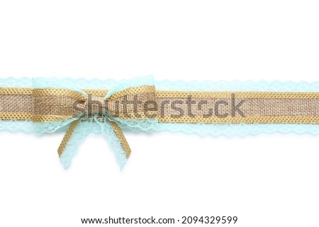 Burlap ribbon and bow with light blue lace on white background, top view
