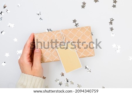 gifts or presents boxes silver confetti on white table top view. female hands in a warm sweater are holding a gift