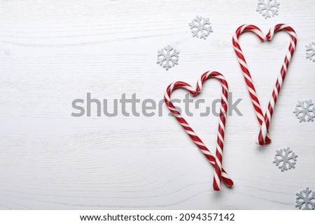 Hearts made of sweet Christmas candy canes and snowflakes on white wooden table, flat lay. Space for text