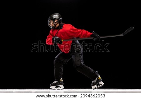Scoring a goal. Portrait of concentrated woman, professional hockey player in motion, training isolated over black background. Concept of sport, action, movement, health. Copy space for ad