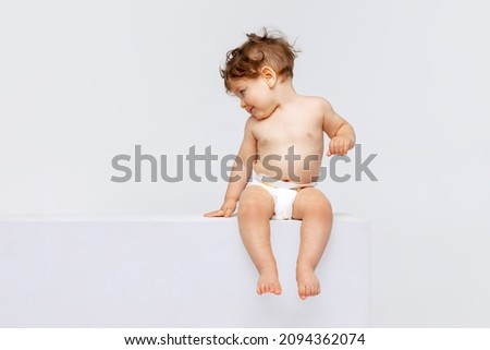 Shy happy child. Portrait of little cute toddler boy, baby in diaper calmly sitting and laughing isolated over white studio background. Concept of childhood, motherhood, life, birth. Copy space for ad Royalty-Free Stock Photo #2094362074
