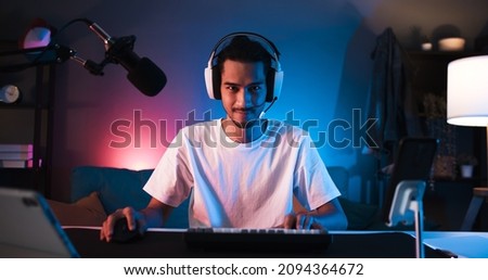 Young confident Asian man playing online computer video game, colorful lighting broadcast streaming live at home. Gamer lifestyle, E-Sport online gaming technology concept Royalty-Free Stock Photo #2094364672