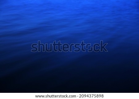 Blue water surface with bright sun light reflections, water in ocean or sea background closeup. Blue sea texture with waves and foam. Blue sea water surface                               