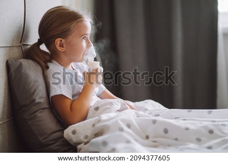 Little girl use inhaler nebulizer lying in bed in bedroom. Child asthma inhaler, nebulizer steam, flu or cold concept. Copyspace Royalty-Free Stock Photo #2094377605