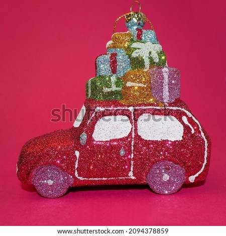 A Christmas tree toy in the form of a pink shiny car with gifts loaded on top stands on a pink background. side view