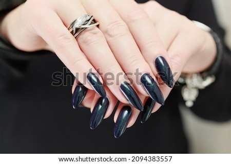 Female hand with long nails and dark purple blue manicure holds a bottle of nail polish