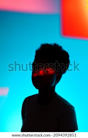 Dark fashion portrait of african american woman with high puff hairstyle and red neon light on face over colorful abstract background. Fashionable studio shot of black millennial girl. Trend and style