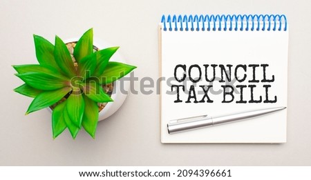 coUNCIL TAX BILL is written in a white notepad near a clipboard, calculator, green plant, glasses and a pen on a yellow and concrete backgroundd.