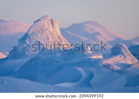 Winter arctic landscape. Ice hummocks and snowdrifts against the background of blurred mountains. Snow-covered ice floes close-up. Cold frosty winter weather. Polar region. Shallow depth of field. Royalty-Free Stock Photo #2094399592
