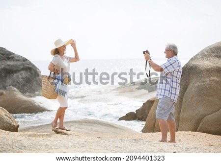 Older man taking pictures of girlfriend on beach