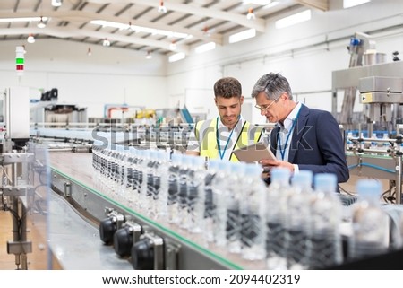 Supervisor and manager watching plastic bottles on conveyor belt