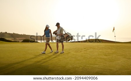 Caddy and woman walking on golf course overlooking ocean Royalty-Free Stock Photo #2094409006