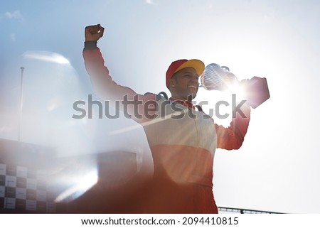 Cheering racer holding trophy on track Royalty-Free Stock Photo #2094410815
