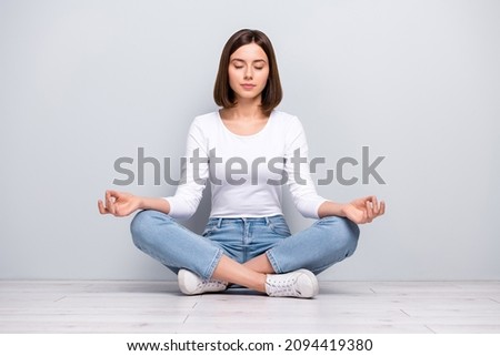 Photo of dreamy peaceful young woman wear white outfit sitting legs crossed practicing yoga smiling isolated concrete grey wall background