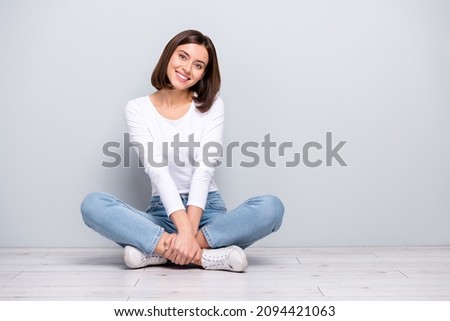Photo of sweet dreamy young lady dressed white clothes smiling sitting legs crossed empty space isolated concrete grey wall background Royalty-Free Stock Photo #2094421063