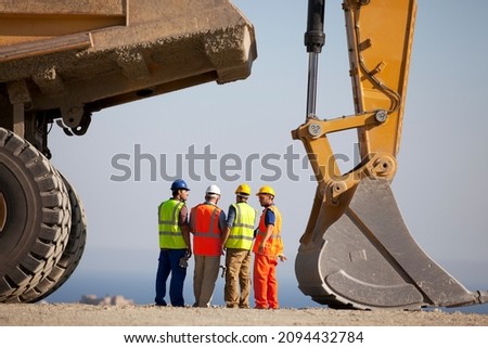 Workers talking by machinery in quarry