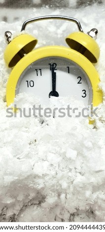 Yellow alarm clock in the snow. New Year and Christmas background. Time is midnight on the clock.