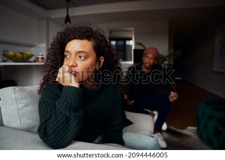 Multi-cultural female ignoring black boyfriend while fighting on the sofa in modern apartment Royalty-Free Stock Photo #2094446005