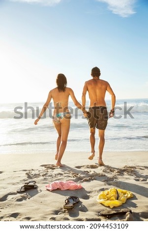 Couple holding hands and walking toward ocean on beach
