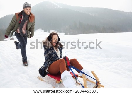 Enthusiastic couple sledding in snowy field