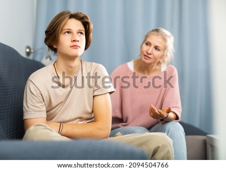 Portrait of upset and offended teenager sitting on sofa while mother soothing him. Mood swings and puberty concept Royalty-Free Stock Photo #2094504766