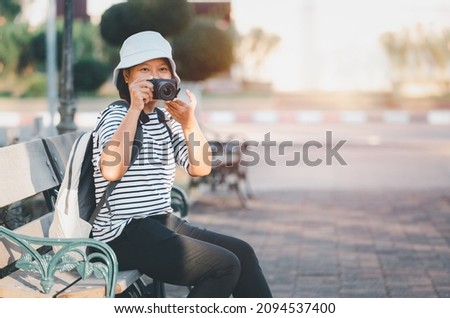 Asian woman tourist with backpacker sitting relexing take photo camera copy space concept , Female sit on city park hand holding camera take photo retro picture style with holiday travel concept.