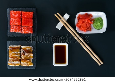 on a black table, top view, rolls with eel, teriyaki sauce, sesame seeds, flying fish caviar, wooden sticks and seasonings, soy sauce, ginger and wasabi