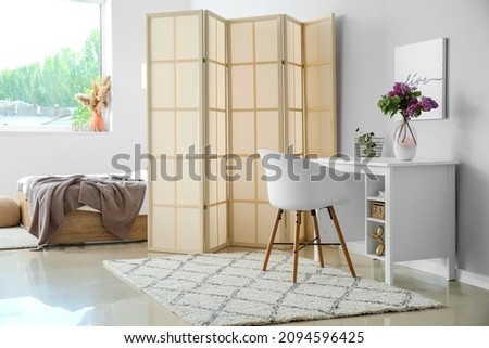 Interior of light room with bed, folding screen and modern workplace Royalty-Free Stock Photo #2094596425