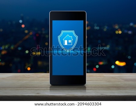 House with shield flat icon on modern smart mobile phone screen on wooden table over blur colorful night light city tower and skyscraper, Business home insurance and security online concept