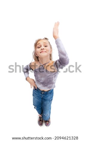 Raising hand up. High angle view of beautiful little girl, kid in casual clothes having fun, posing isolated on gray studio background. Concept of emotions, childhood, facial expression