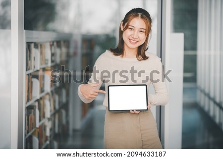 Portrait of a young Asian female college student showing a blank screen portable tablet. business and technology