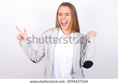 Cheerful Curious Young business woman wearing grey jacket over white background showing copy space ad celebrating luck