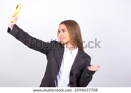 Portrait of a Young business woman wearing jacket over white background taking a selfie to send it to friends and followers or post it on his social media.
