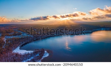 Aerial view of the winter background with a snow-covered forest, lake and sunrays over the Glukas lake in Lithuania Royalty-Free Stock Photo #2094640150
